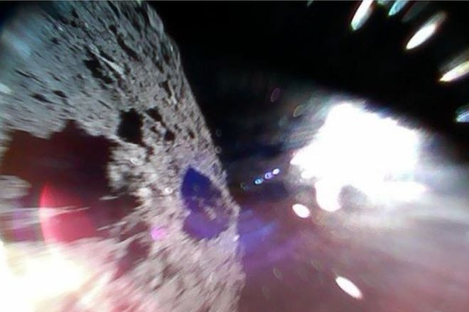 Picture shows the surface of the asteroid on the left and a white sun glare on the right