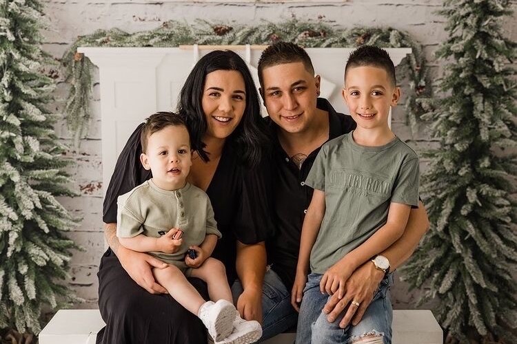 A mum, dad and two boys pose for a family photo wearing green, black and denim.