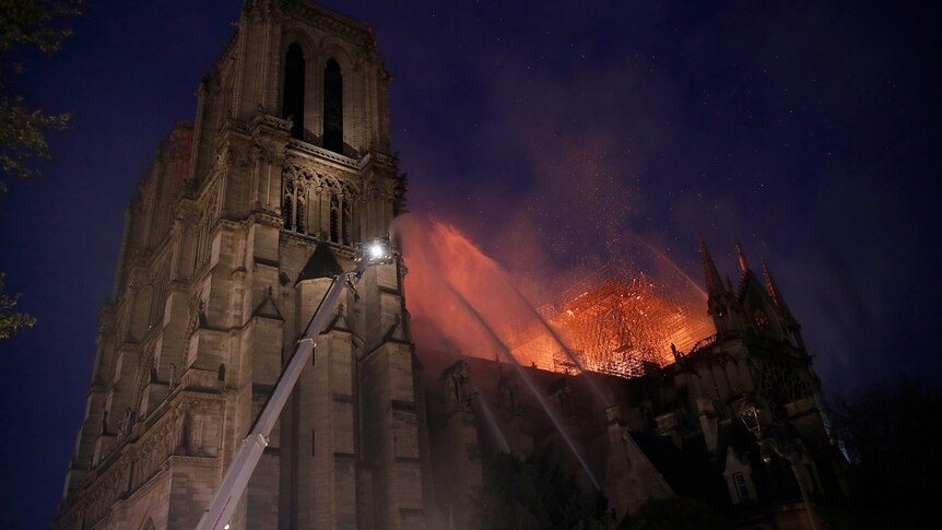 Firefighters spray water up at the burning roof of a large cathedral as embers drift into in the darkening sky