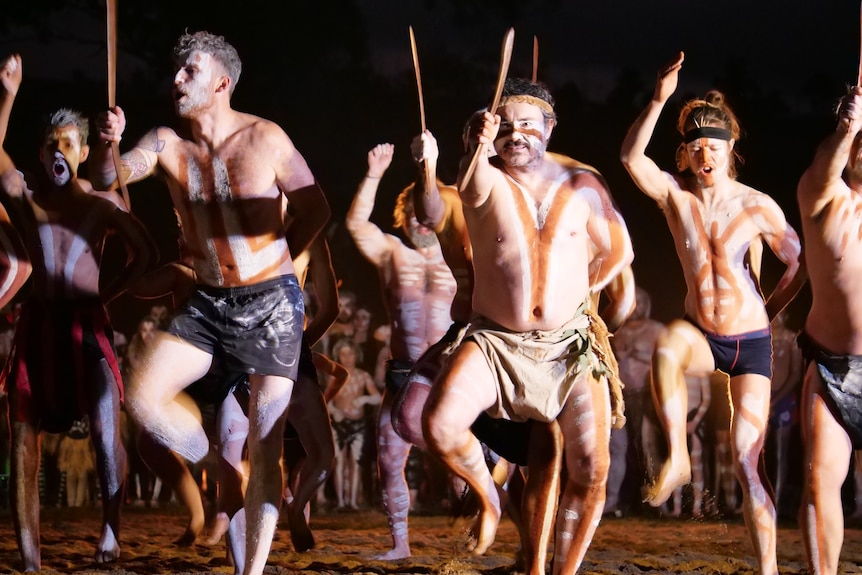 Men in traditional paint wearing no shirts dancing.