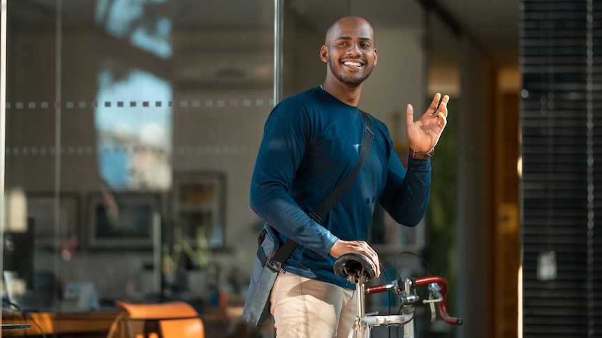 man waving to his colleagues as he leaves work on a bike