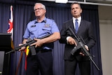 Chris Dawson and Paul Papalia standing next to each other holding guns—one is real and one is a gel blaster