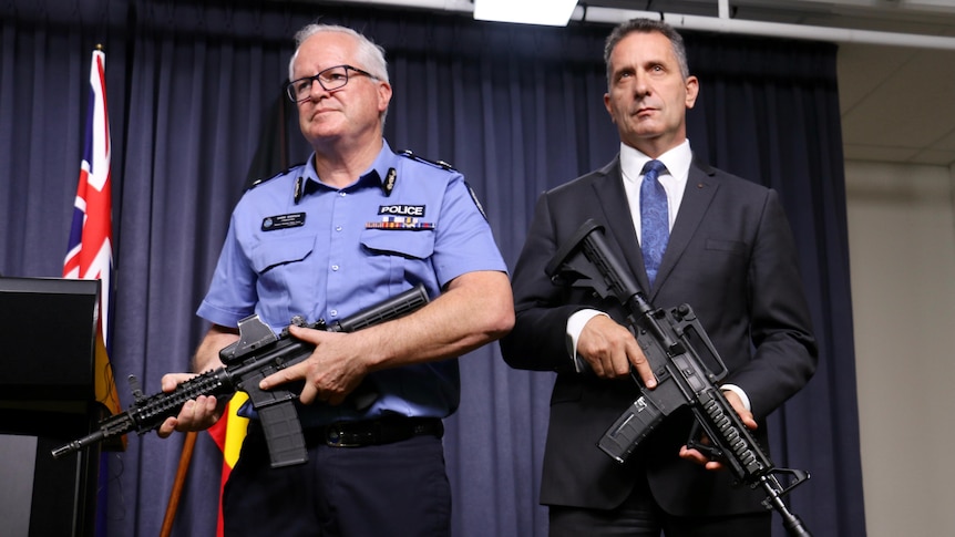 Chris Dawson and Paul Papalia standing next to each other holding guns—one is real and one is a gel blaster