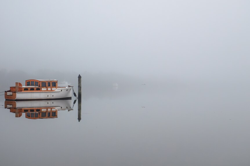 A small boat hitched to a pole in a river surrounded by white fog 