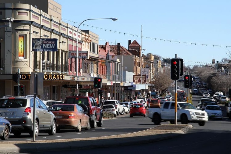 A country town street with traffic lights, cars and buildings.