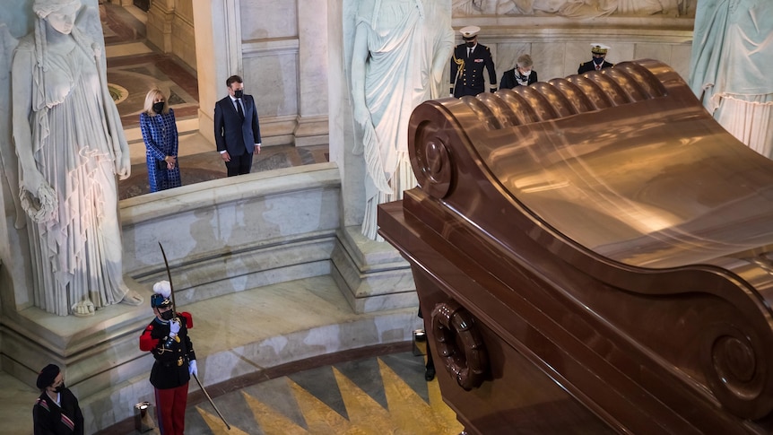 officials stand around a large brown tomb 