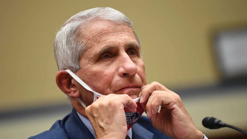 Dr Anthony Fauci, taking off his mask to speak into a microphone at a hearing in Washington.