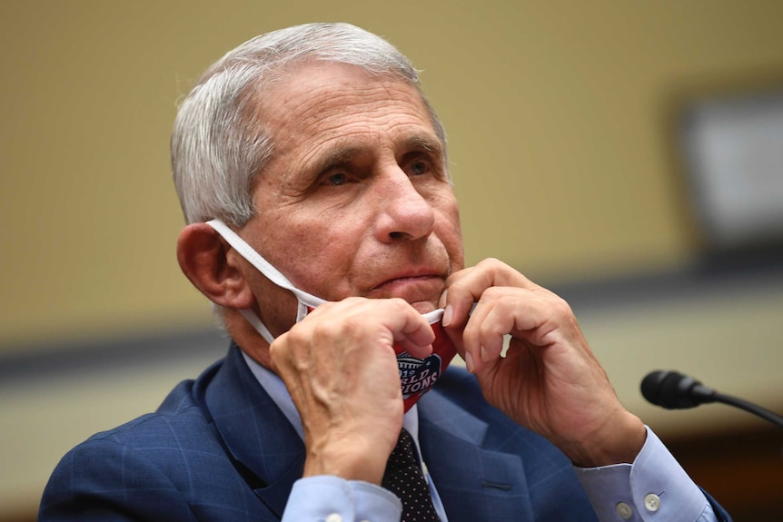 Dr Anthony Fauci, taking off his mask to speak into a microphone at a hearing in Washington.