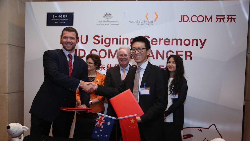 Two men shake hands while holding Chinese and Australian flags with Trade Minister Andrew Robb in the background