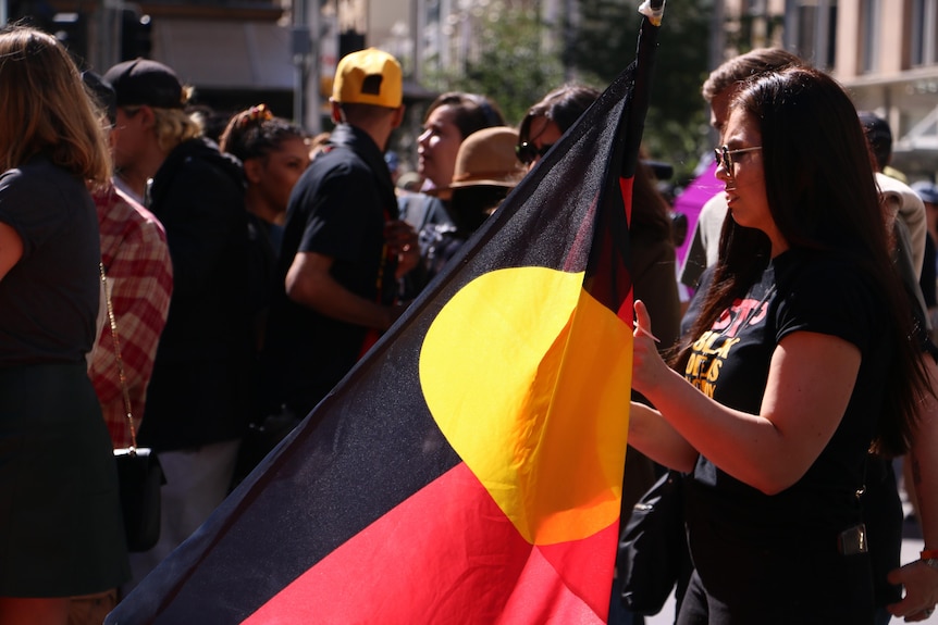 a woman in a crowd holding an aboriginal flag