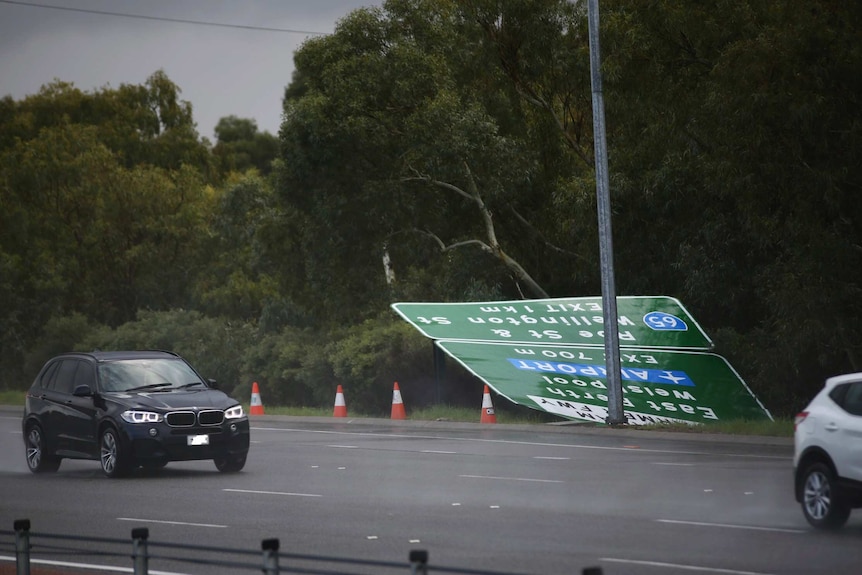 A large street sign has fallen on the side of the side of the Mitchell Freeway. There are orange cones around it.