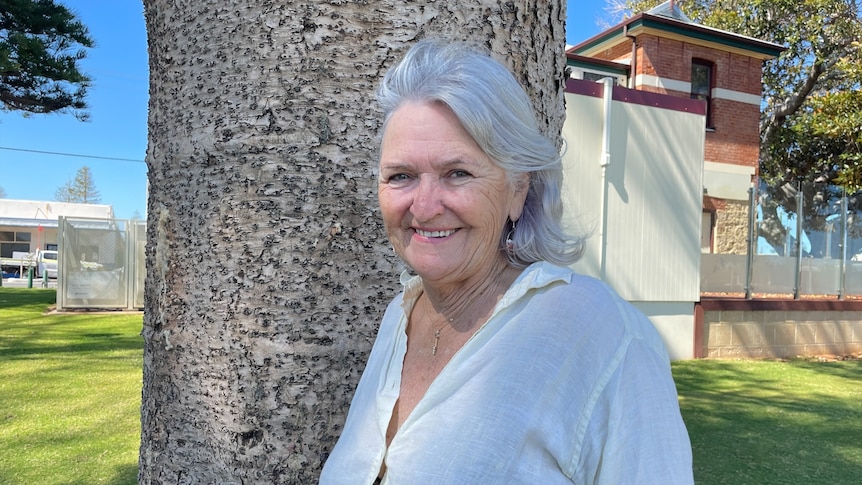 Grey haired woman smiling near tree