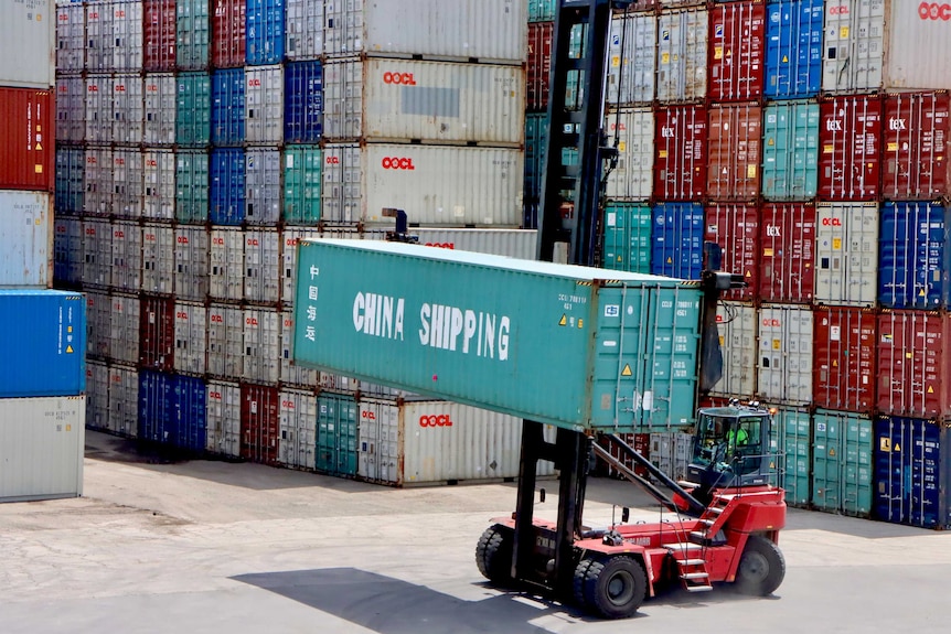 A forklift moves a China Shipping container at Port Botany, in front of a large stack of other containers.