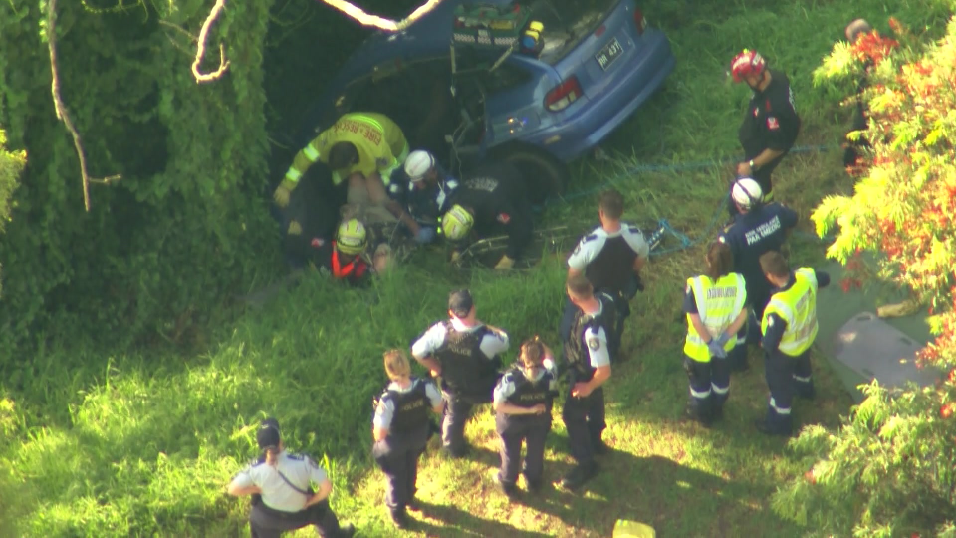 Firefighters help drag a man out of a crumpled blue car in a ditch