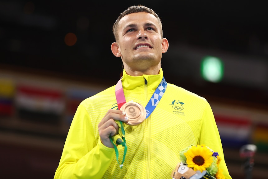 An Australian male boxer holds up his bronze medal at the Tokyo Olympics.
