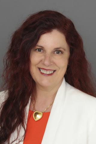 Una mujer de largo cabello rojo y ojos marrones sonríe a la cámara.