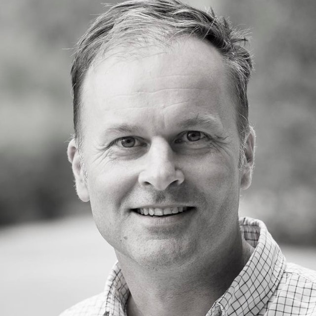 A black and white portrait of a man with short brown hair, looking at the camera.