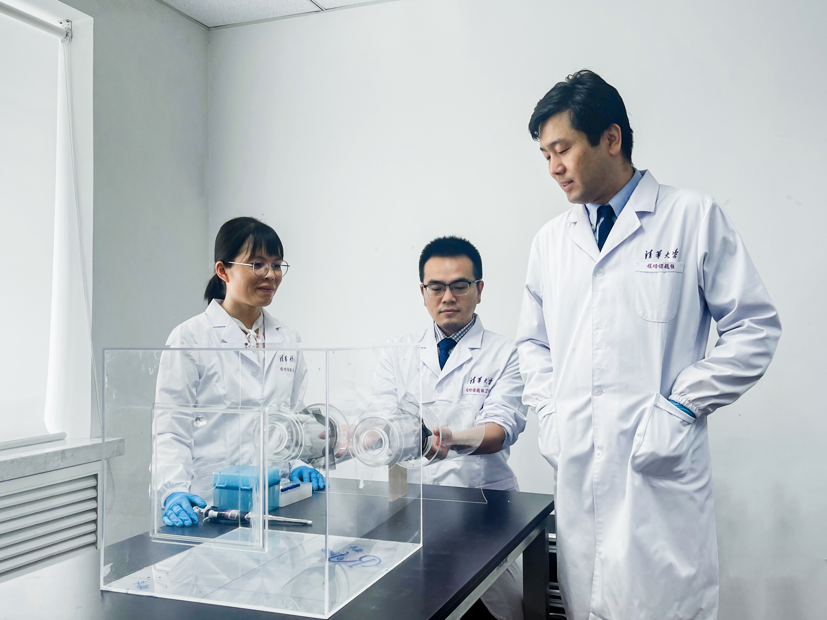 Asian scientists in lab coats standing around a clear plastic box
