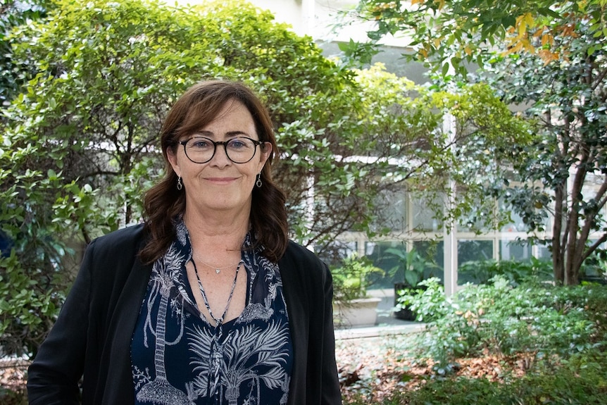 Woman standing in front of trees looks at the camera