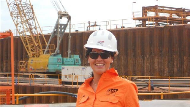 Jenny on a work site wearing an orange uniform and hard hat