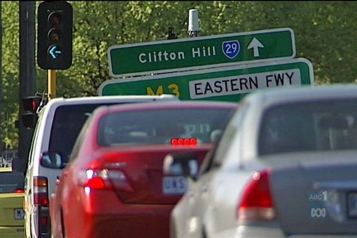 Cars on a road in front of a green sign.