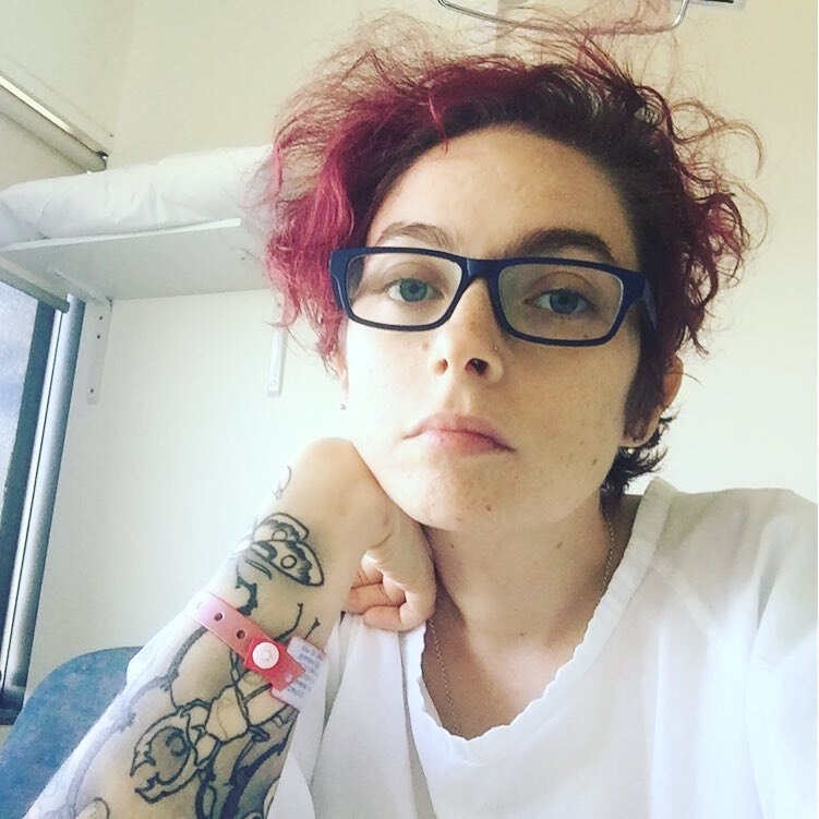 Woman with red hair, spectacles and tattooed arm looks into camera