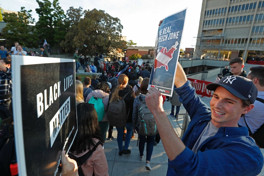 A man holding a sign reading 'The Real Free Speech Zone' confronts a man holding a 'Black Lives Matter' placard.