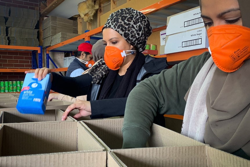 Women wearing headscarves packing boxes in a warehouse.