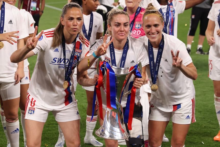 Three women athletes pose with a trophy after winning a major competition.