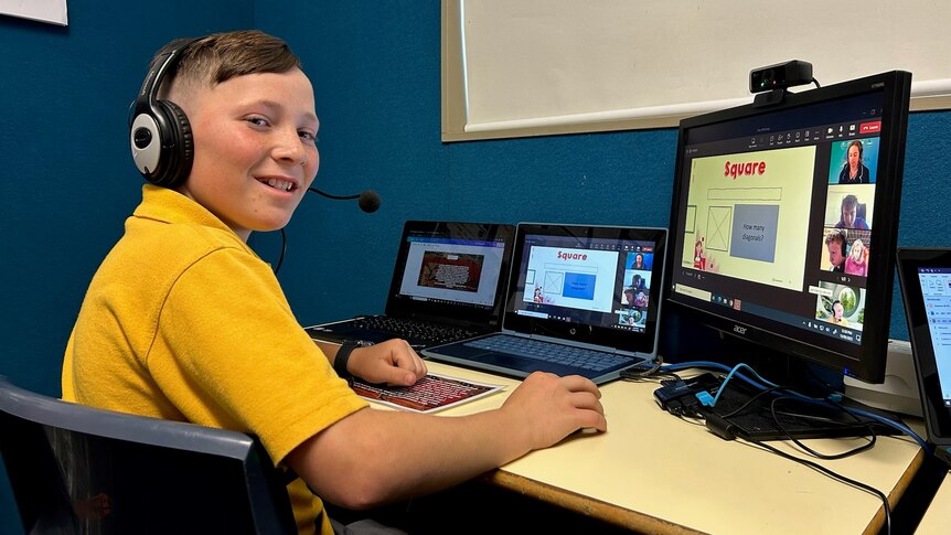 A boy smiles while working on his computer. 