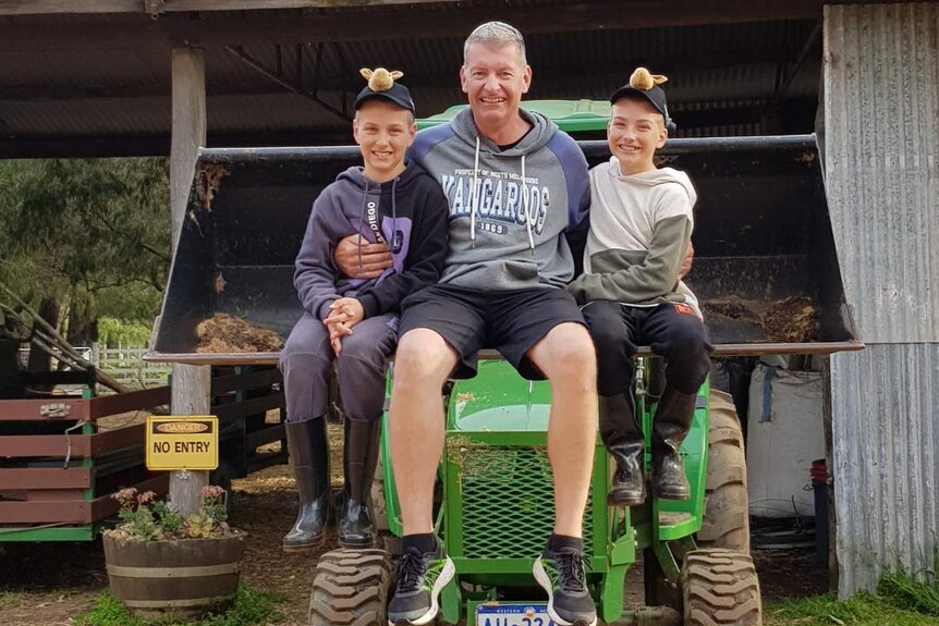 Mr Mason sits on a tractor with his arms around his two sons David and Kallan..