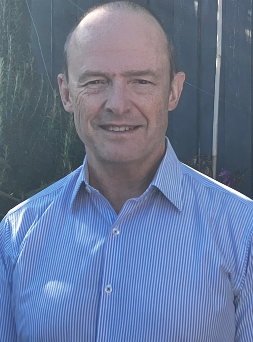 A balding man with cropped hair, wearing a striped button-down shirt. 