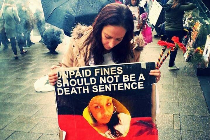 Alira Kelly-Ryder holding a sign protesting against laws which send fine defaulters to prison.