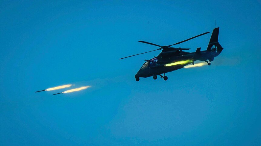 Wide shot of a helicopter shooting missiles.