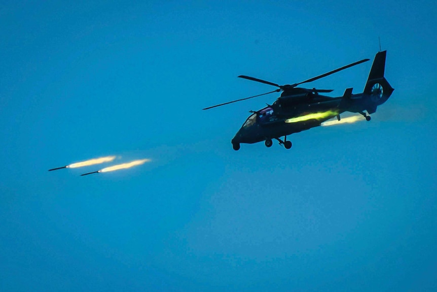 Wide shot of a helicopter shooting missiles.