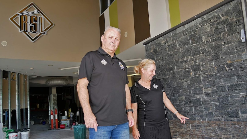 A man looks at the camera while a woman looks at the bricks