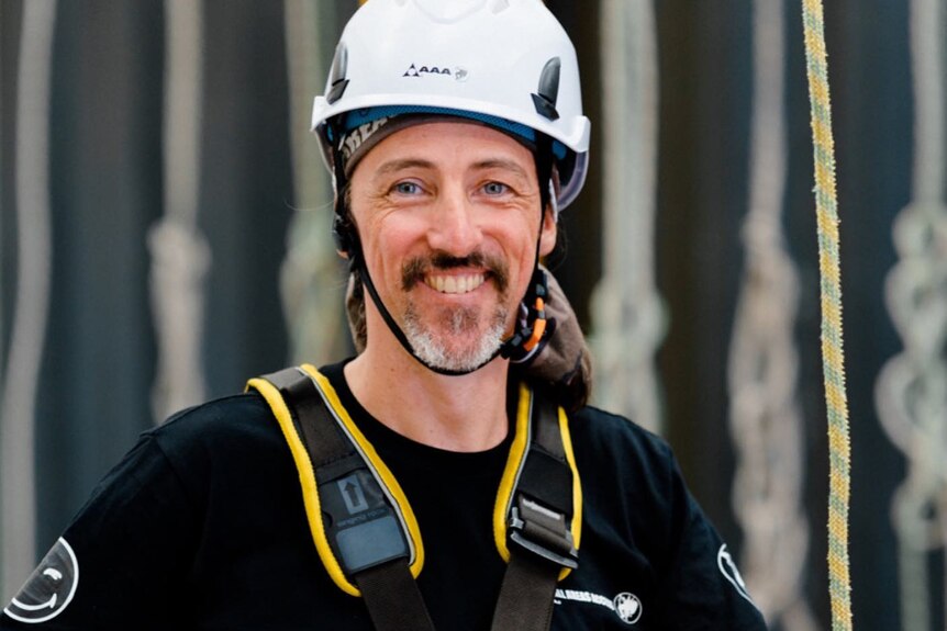 A man smiles while dressed in climbing gear.