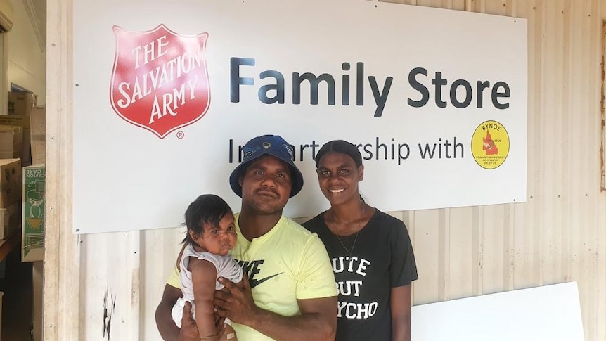 A young Aboriginal family stands infront of a big sign that reads Salvation Army Family Store