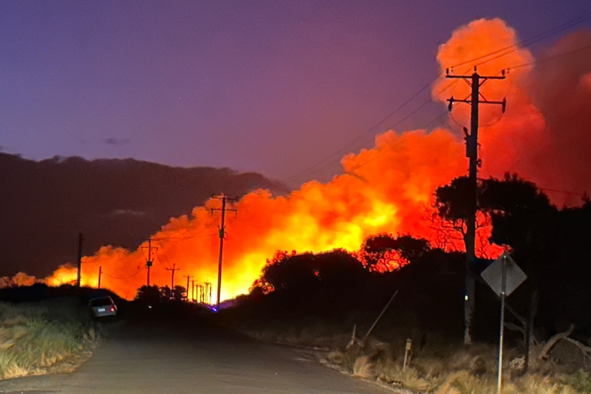 A huge bushfire burns across a road at night.