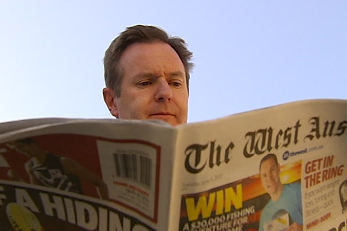 Paul Armstrong's head shows above an unfolded copy of the West Australian newspaper.