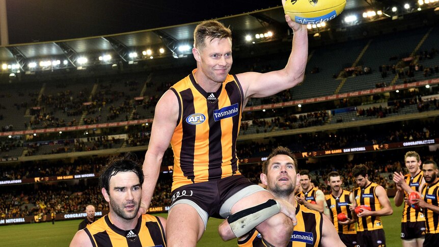 Sam Mitchell of the Hawks is carried from the MCG by Jordan Lewis and Luke Hodge while carrying a yellow football.