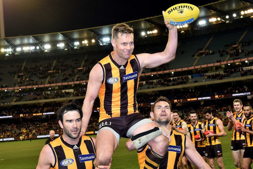 Sam Mitchell of the Hawks is carried from the MCG by Jordan Lewis and Luke Hodge while carrying a yellow football.