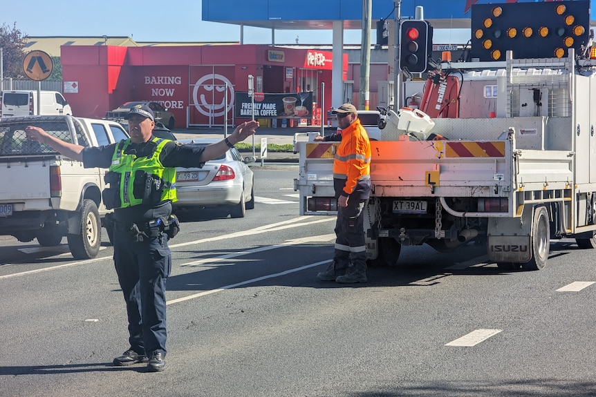 A police office stands amid traffic with arms outstretched.