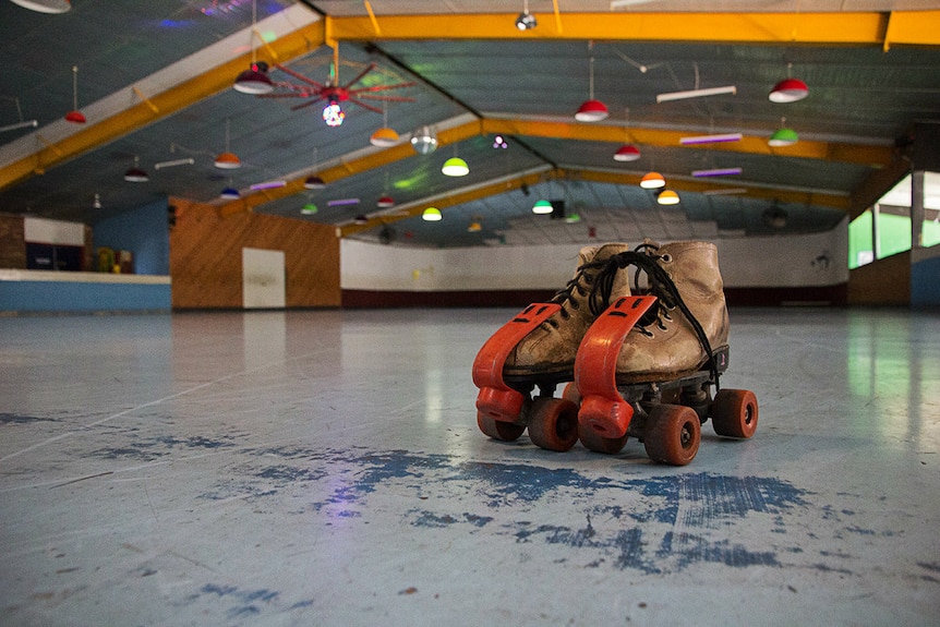 A pair of old leather rollerskates on a blue cement floor
