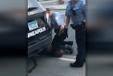 A white police officer kneels on the neck of a prone black man in a US city.