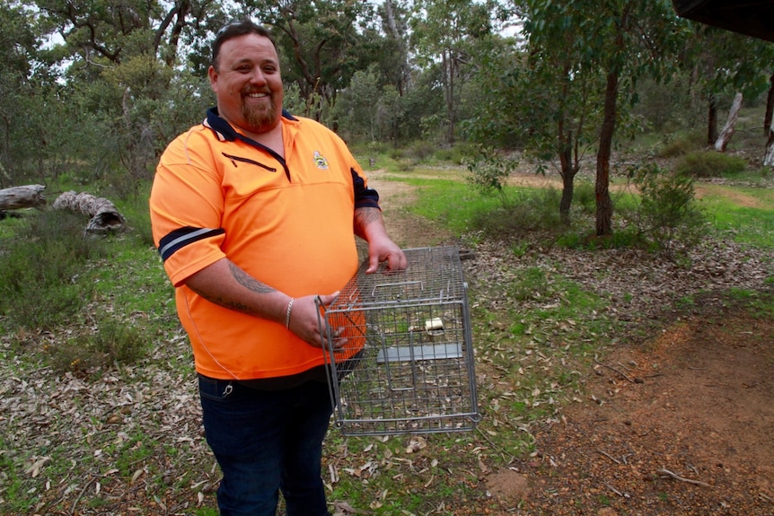 Ranger Guy Maley stands with a cat trap in the bushland.