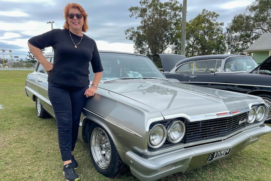 Lady standing next to silver classic car.