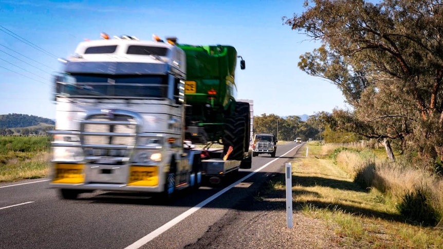 A truck carrying a header is driving along a highway