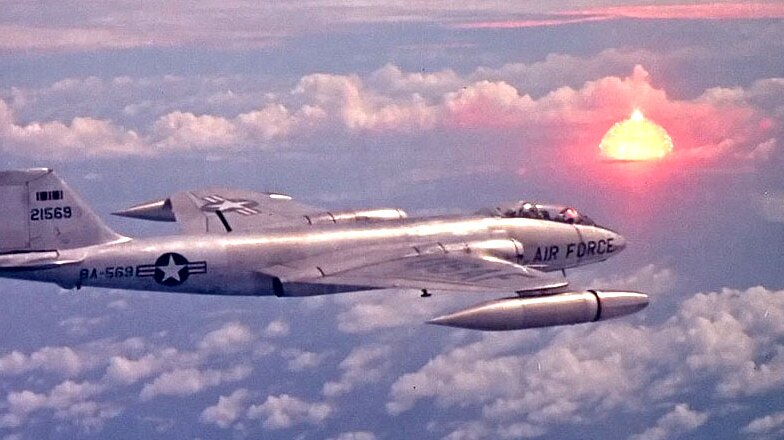 A US Air Force plane with the bright cloud of the nuclear explosion in the distance.