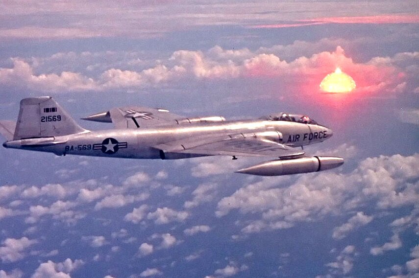 A US Air Force plane with the bright cloud of the nuclear explosion in the distance.